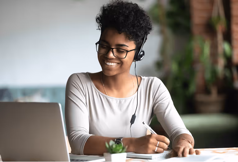 Smiling remote worker with headset taking notes during online meeting