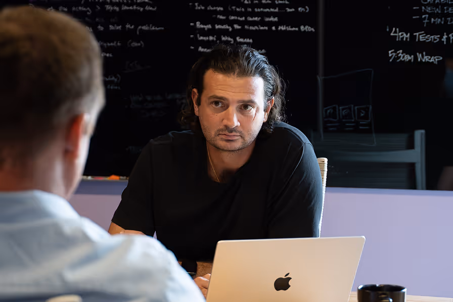 Focused professional working on MacBook during team strategy meeting at ShyftOff