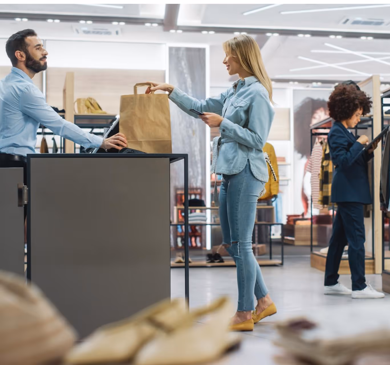 Retail store cashier handing shopping bag to customer at checkout counter
