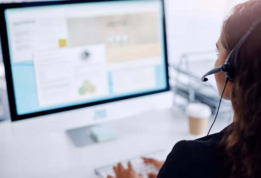 Woman in a headset working on a desktop computer with multiple windows open on the screen.