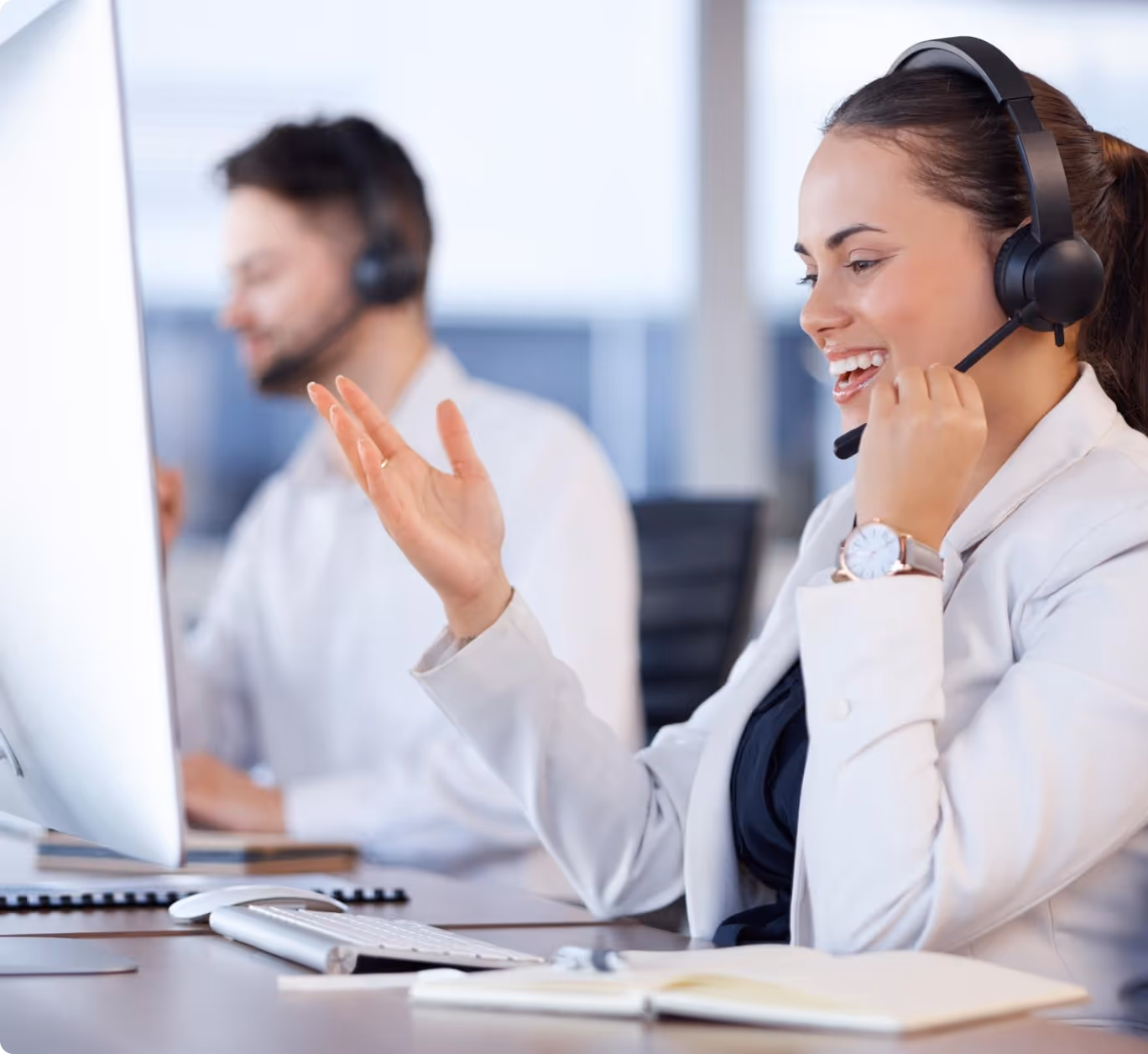 Smiling female call center agent in a headset talking while working on a desktop computer.