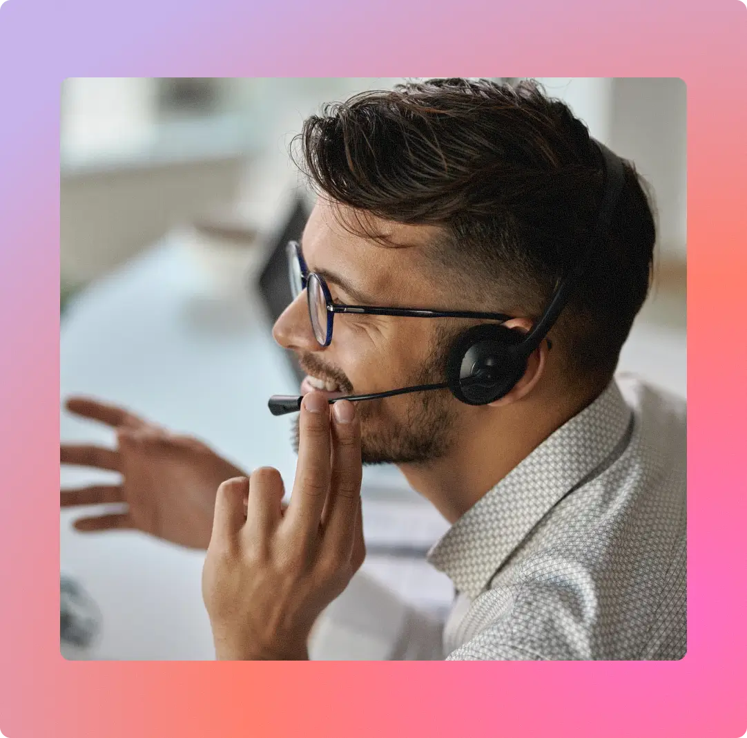 Smiling man wearing glasses and headset, speaking and gesturing with his hand while working.