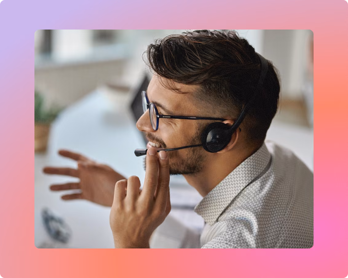 Smiling support agent wearing a headset gesturing while talking to a customer at his desk.