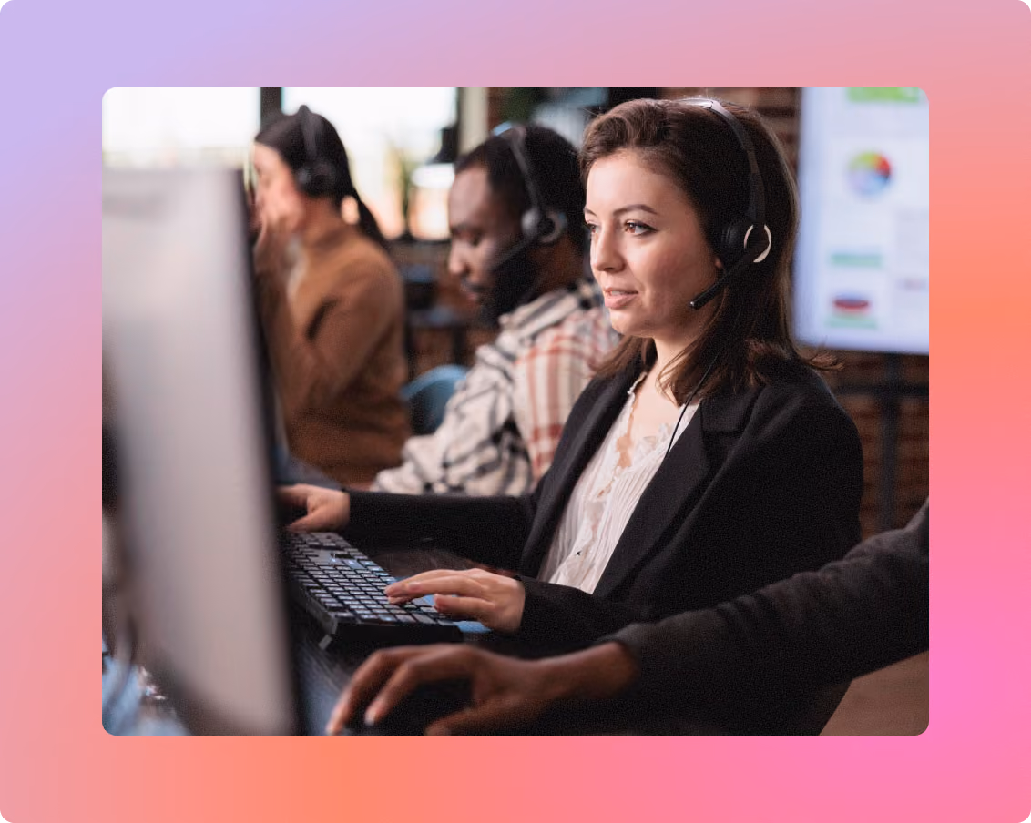 Call center team wearing headsets and working at computers, with a woman in the foreground typing at her keyboard.