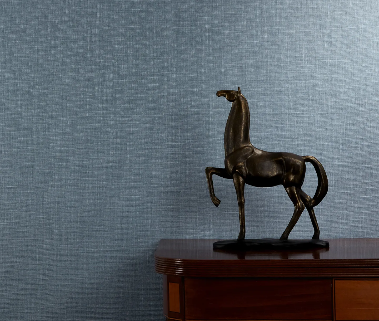 Modern sculpture of a horse on a side table, styled against a blue luxury wallcovering.