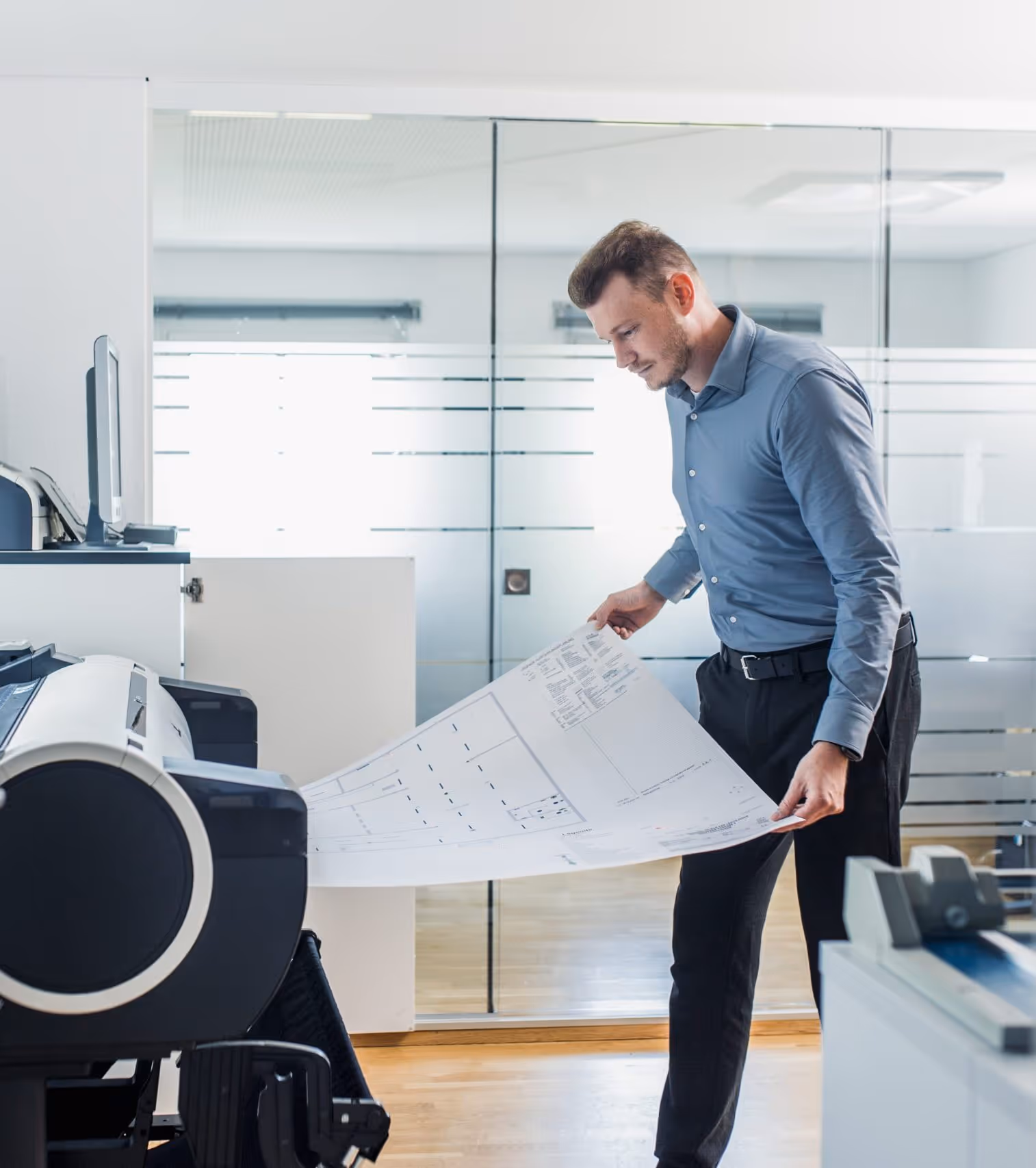 Ein Mann im Büro, der einen großen Papierbogen aus dem Drucker zieht, auf dem ein Grundriss und weitere Plandetails zu sehen sind.