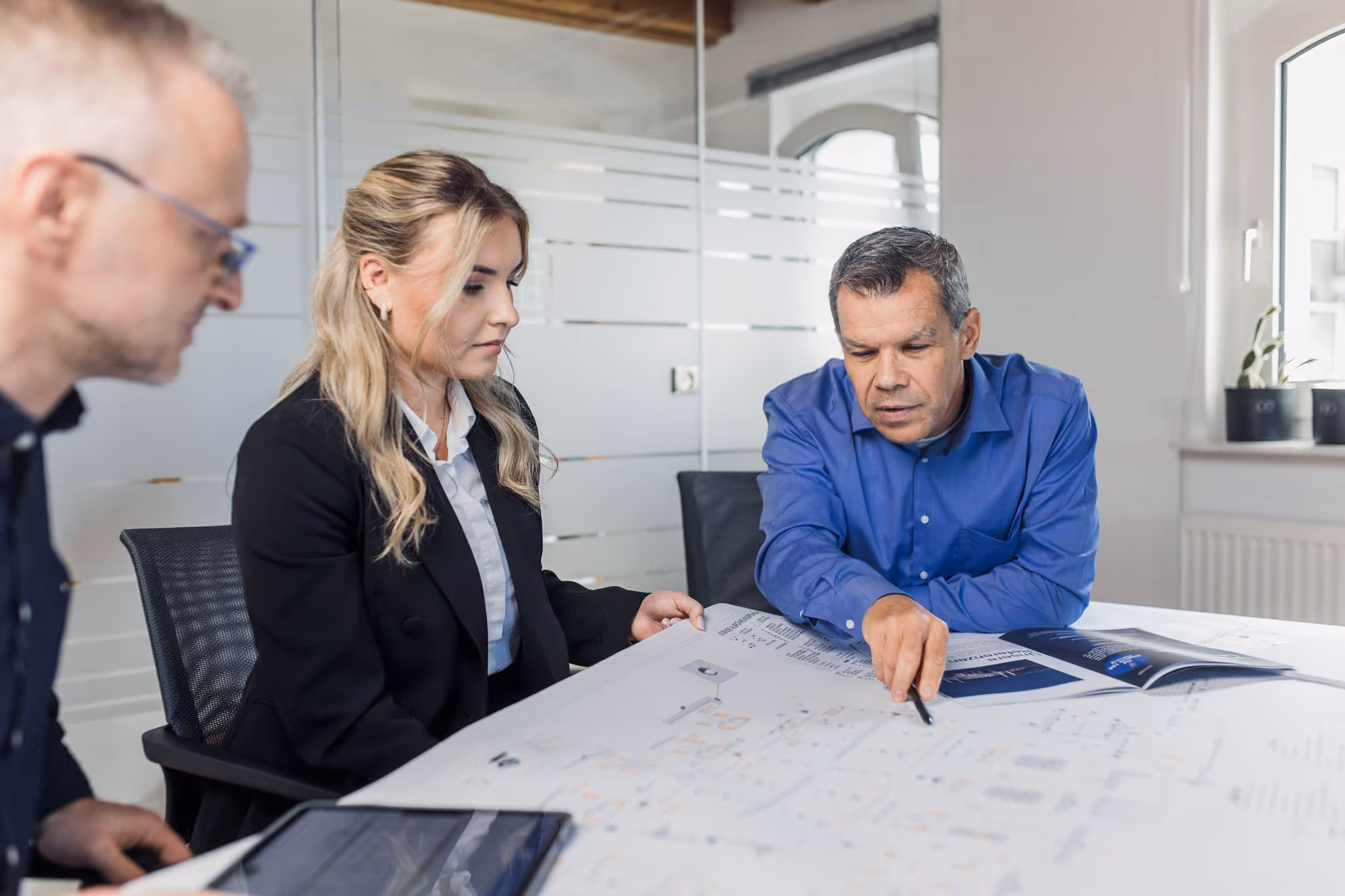 3 MBS-Mitarbeiter, die im Büro einen auf dem Tisch ausgebreiteten Plan besprechen.