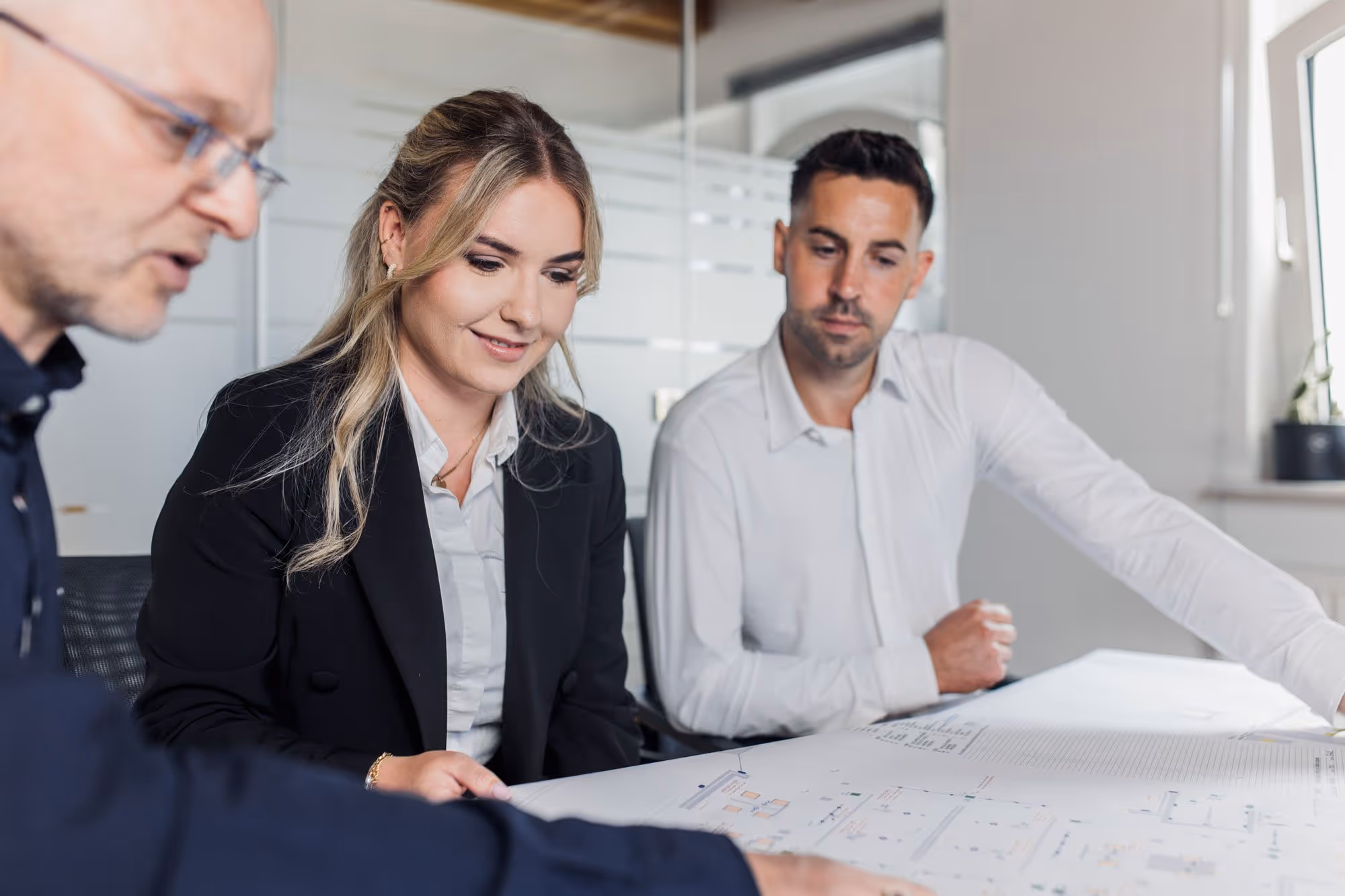 3 MBS-Mitarbeiter, die im Büro einen auf dem Tisch ausgebreiteten Plan besprechen.