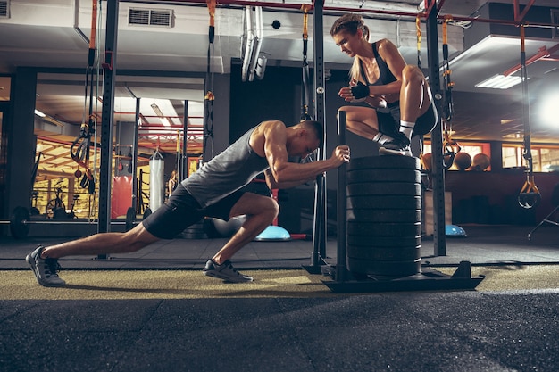a woman squating on weights and helping a man improve his fitness