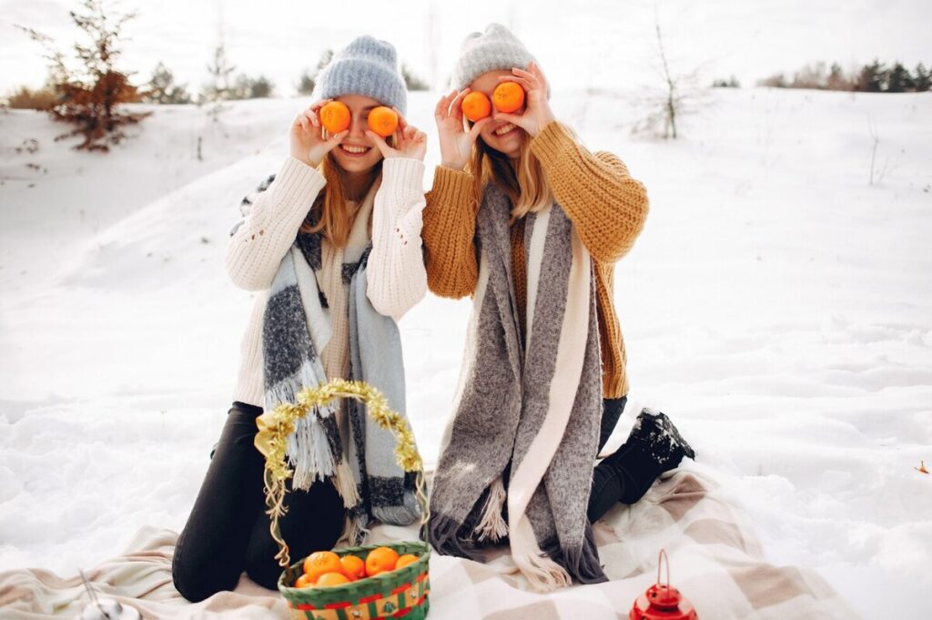 Two girls in the snow with tangerine on their eyes 