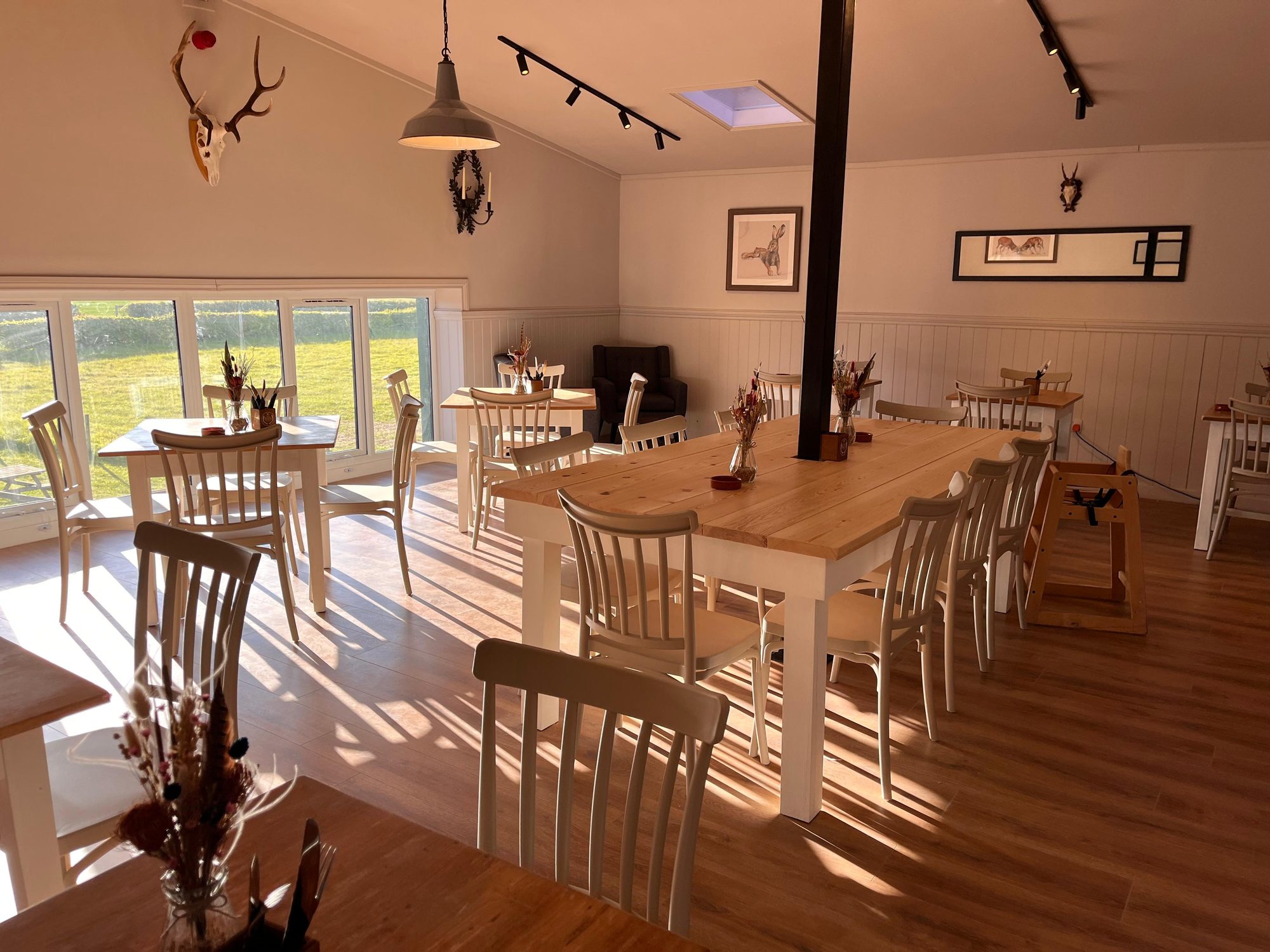 Sunlit dining area at The Barn Kitchen with a long farmhouse table and views over the Suffolk countryside