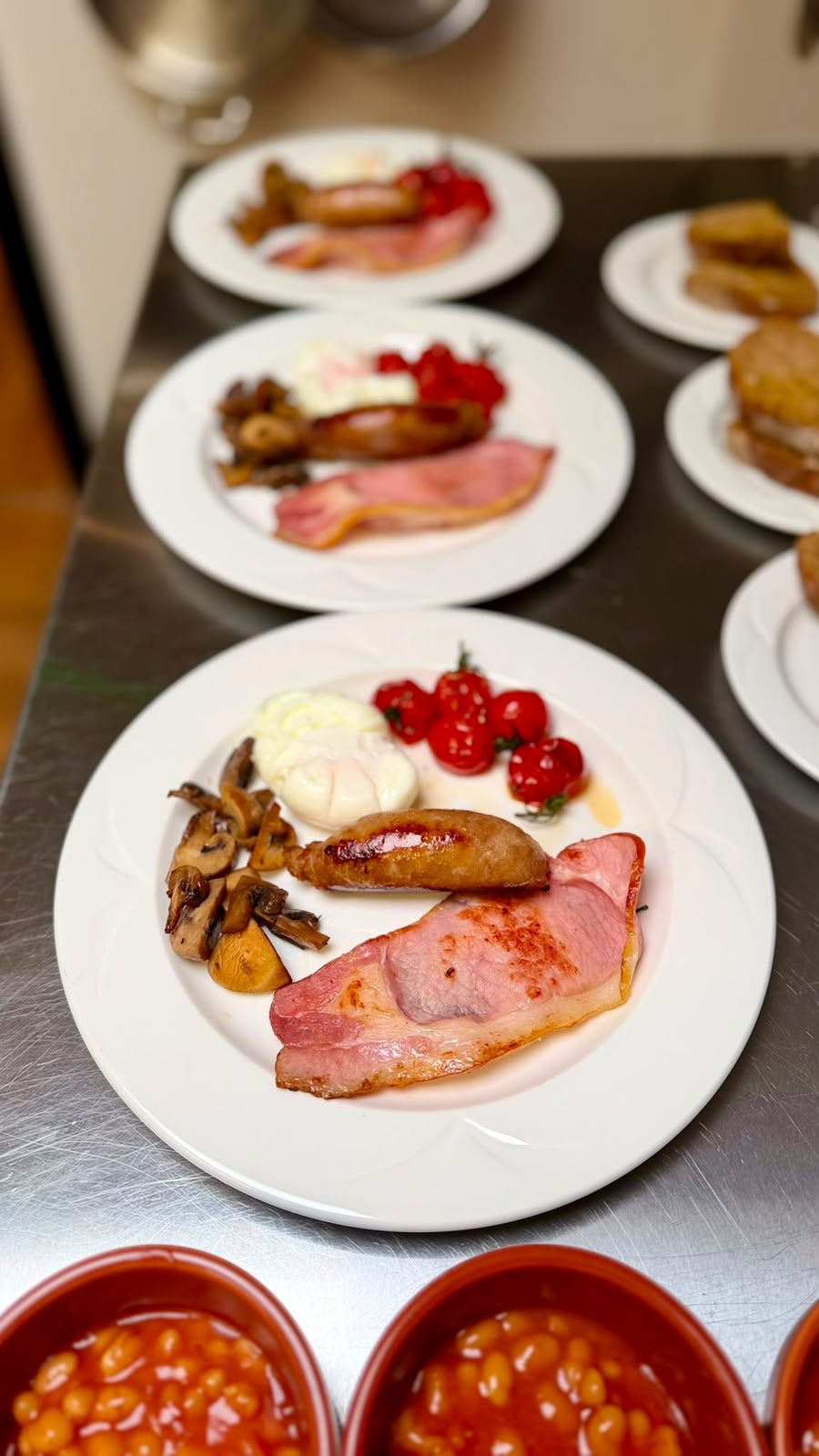 Breakfast plates lined up on the pass at The Barn Kitchen with bowls of baked beans