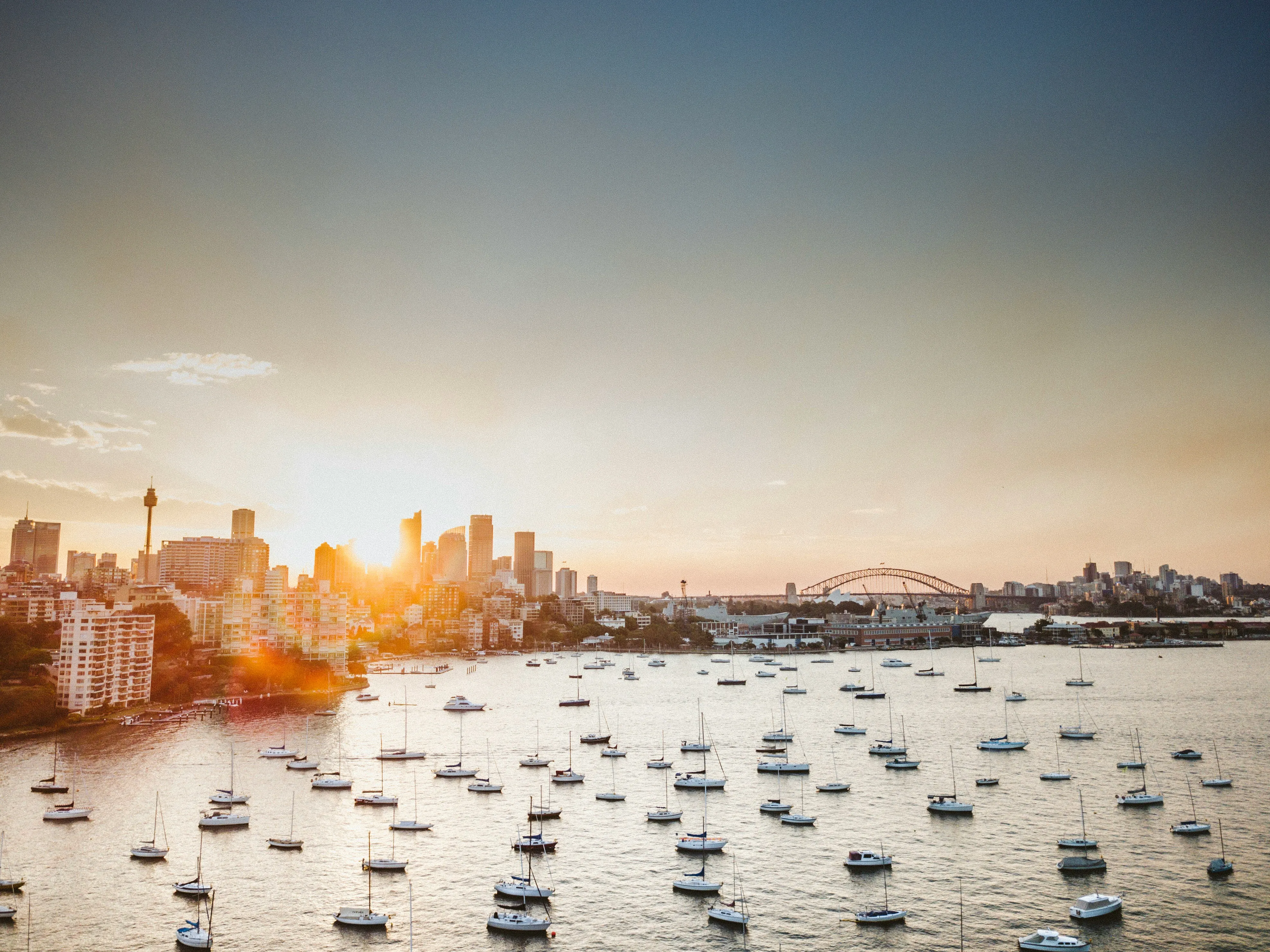 Sunset over Sydney Harbour with moored sailboats, the city skyline and the Harbour Bridge in the distance
