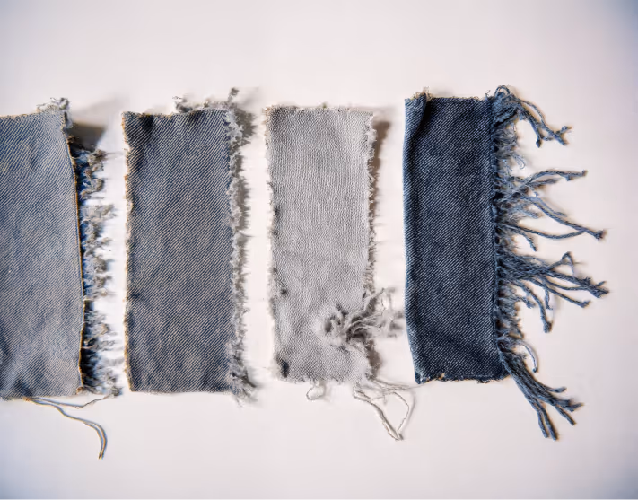 Frayed denim fabric swatches in various washes — textile samples for sustainable jeans production