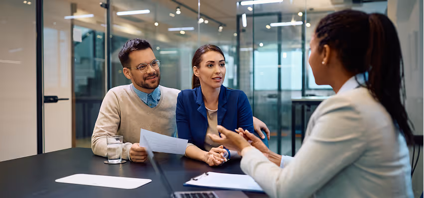 Two people meeting with advisor at a glass-walled office to discuss investment planning