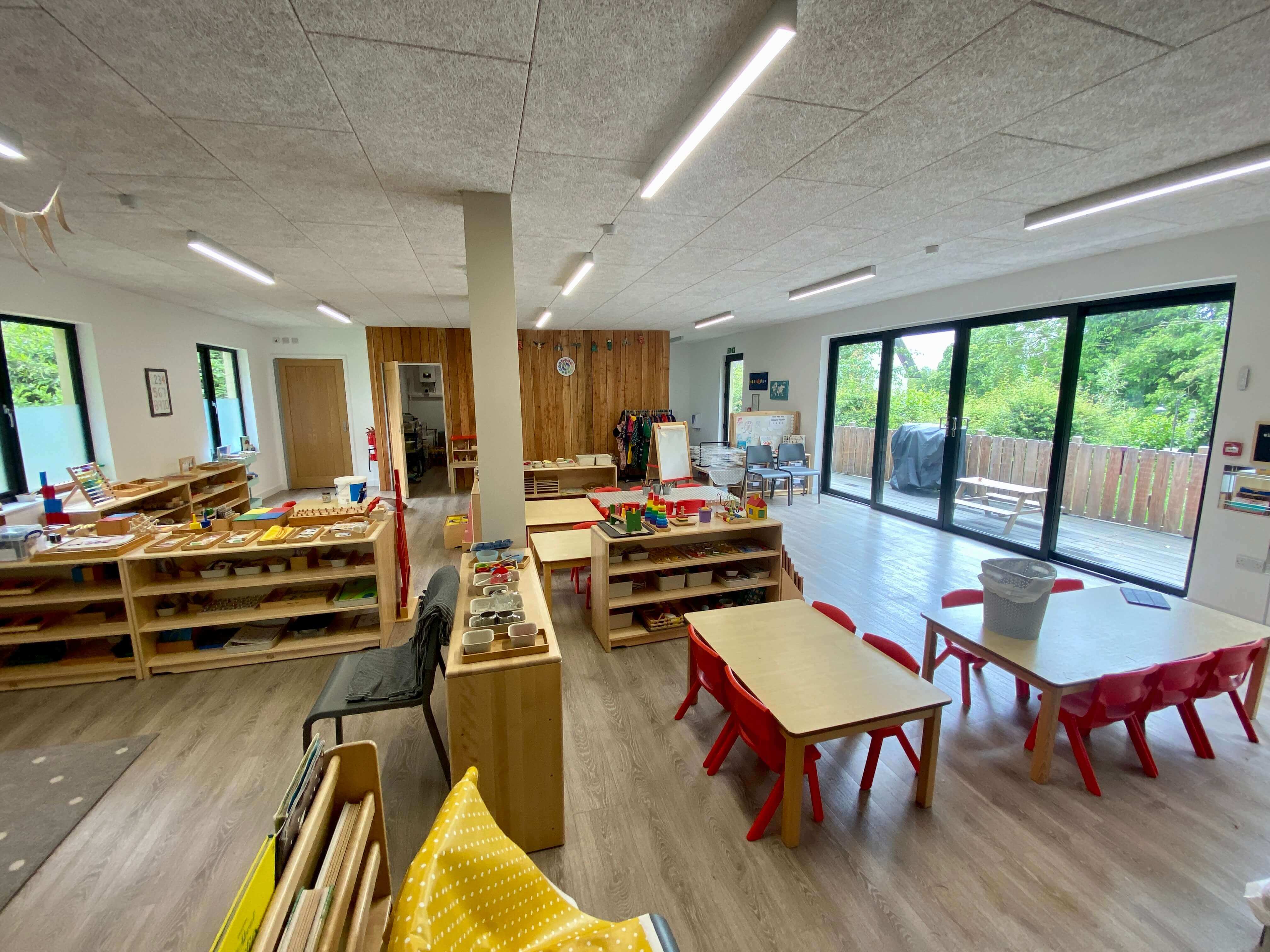 Montessori classroom at Daisies with low wooden shelves, red chairs and full-height glazing