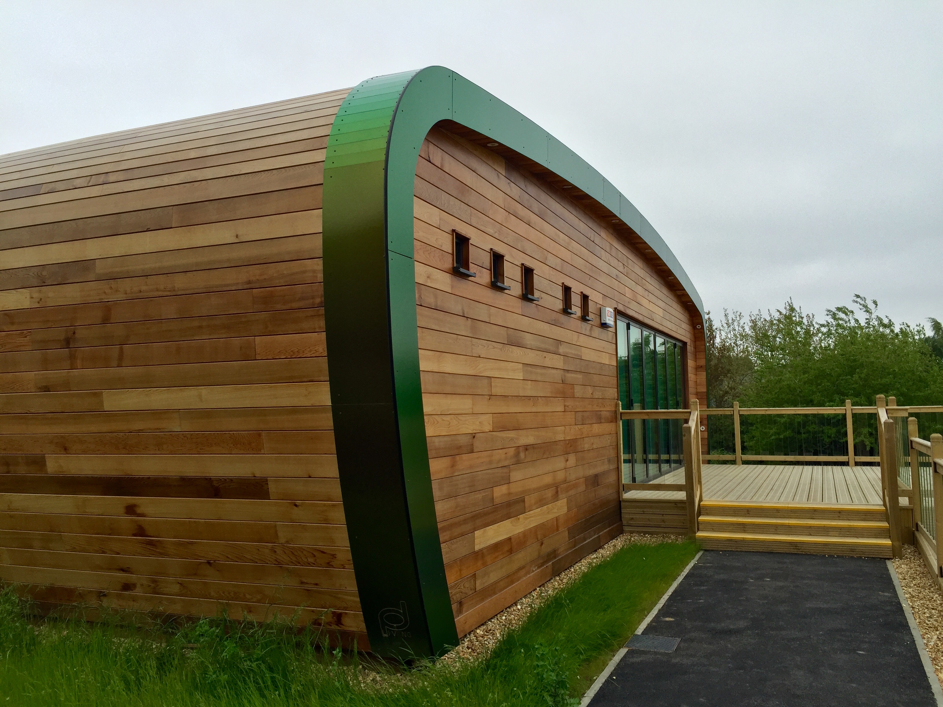 Curved cedar-clad classroom with a green fascia and decking at Canklow Primary