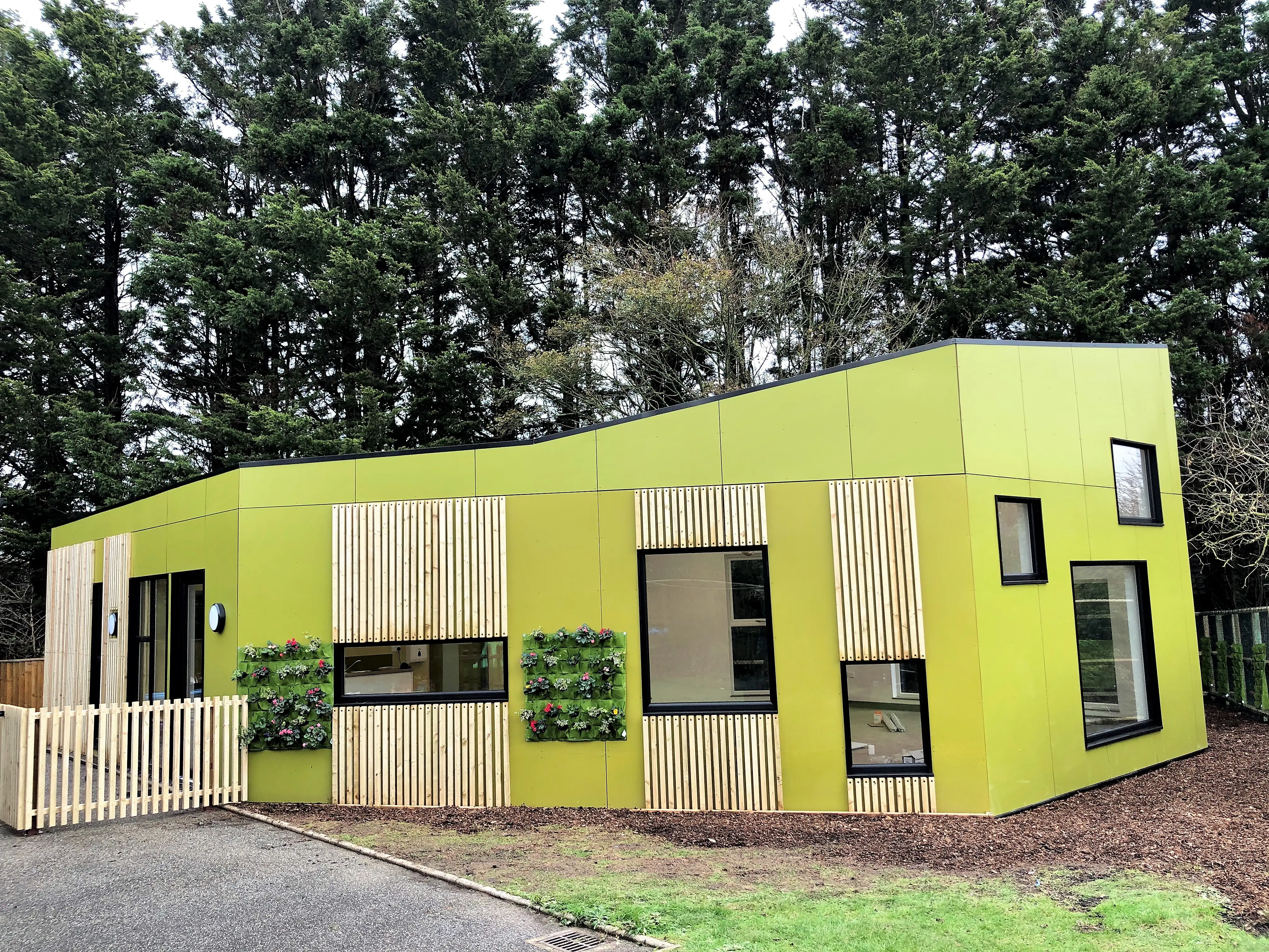 Tops Day Nursery modular building in lime green with timber slat cladding and living wall planters