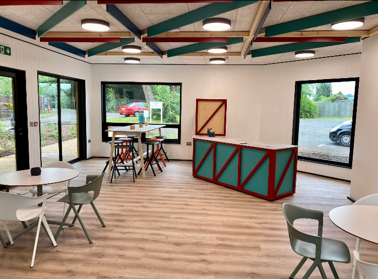 Bright modular community space with a teal counter, round tables and exposed timber beams