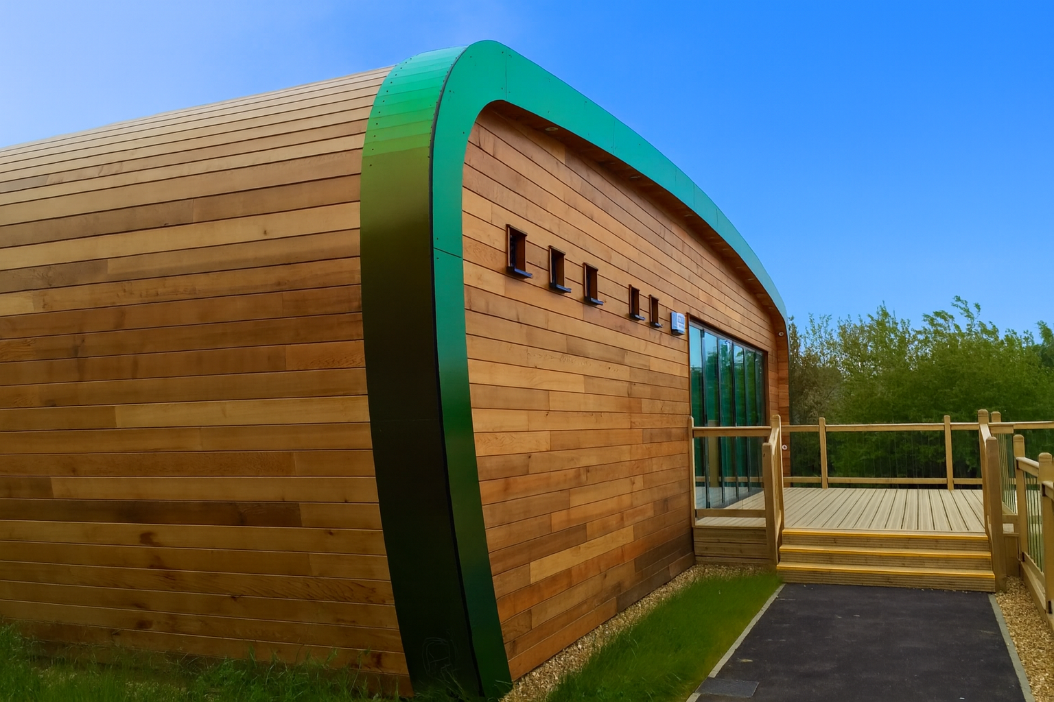 Curved cedar-clad eco classroom with a green fascia and timber decking