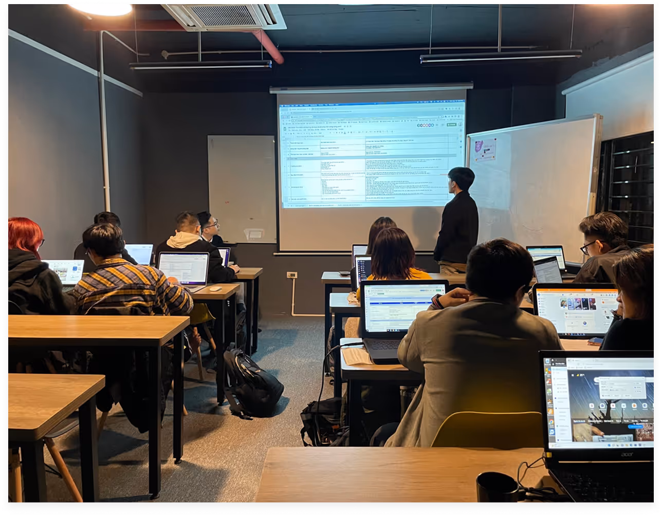 a group of people in a classroom with laptops