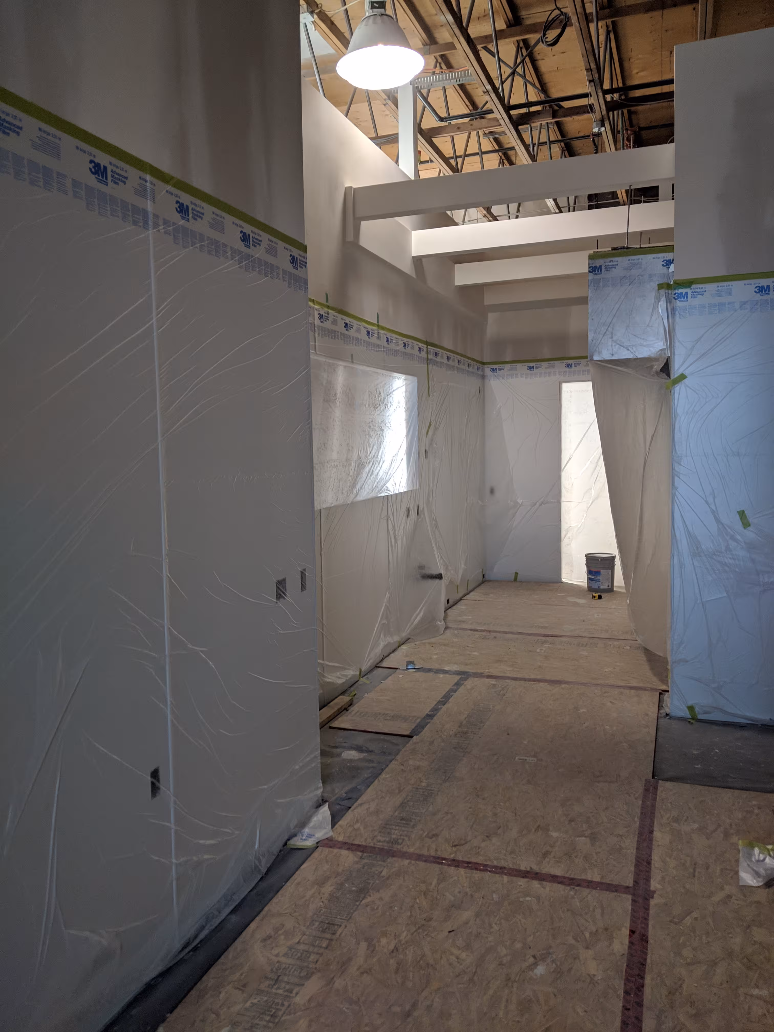 New construction interior prepped for painting, with walls and windows masked in plastic sheeting and floors covered.