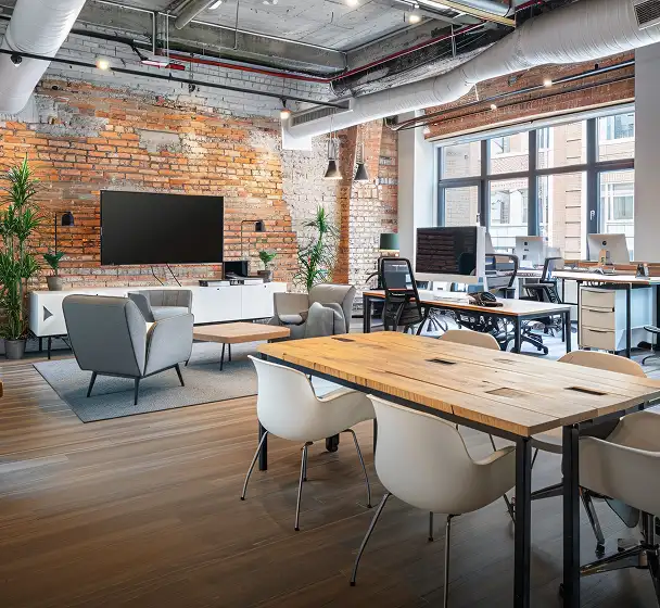 Contemporary open-plan office with brick walls, large windows, and shared desks