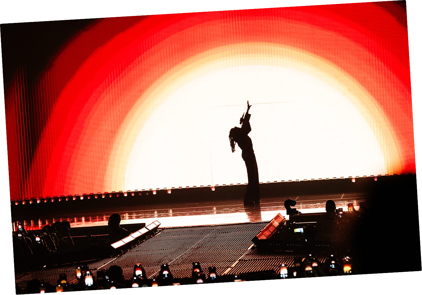 Chanteur sur scène éclairé par plusieurs projecteurs blancs devant un public nombreux dans une salle sombre.