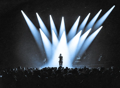 Chanteur seul sur scène illuminé par de puissants projecteurs blancs devant un large public.