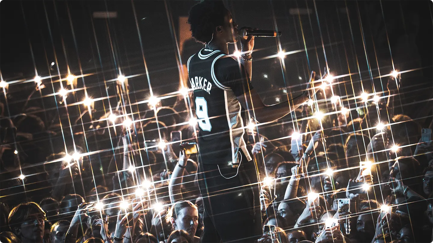 Chanteur sur scène avec un maillot numéro 9, face à une foule tenant des téléphones allumés lors d’un concert nocturne.