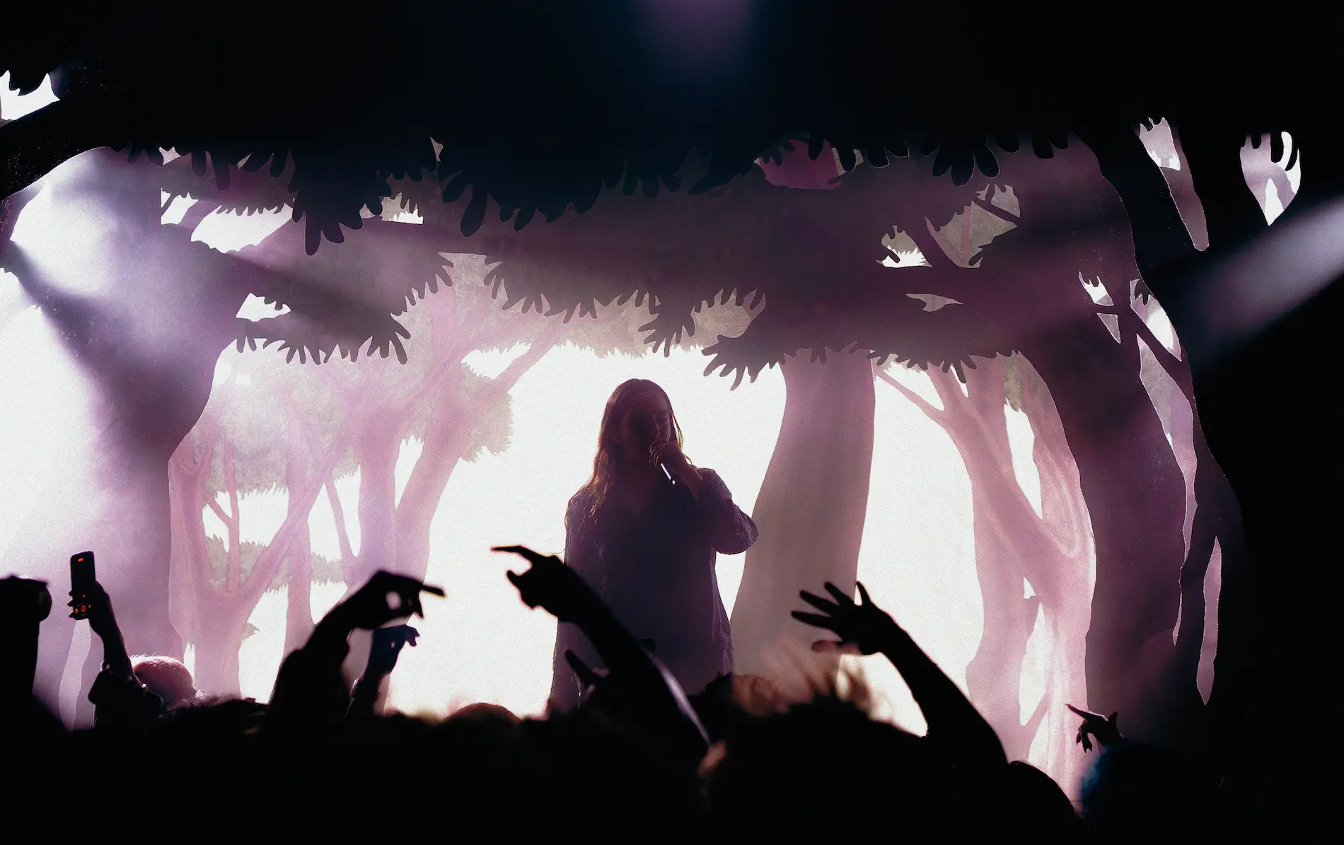 Jeune homme aux yeux bleus intenses, cheveux noirs bouclés, portant une veste beige et deux chaînes au cou.