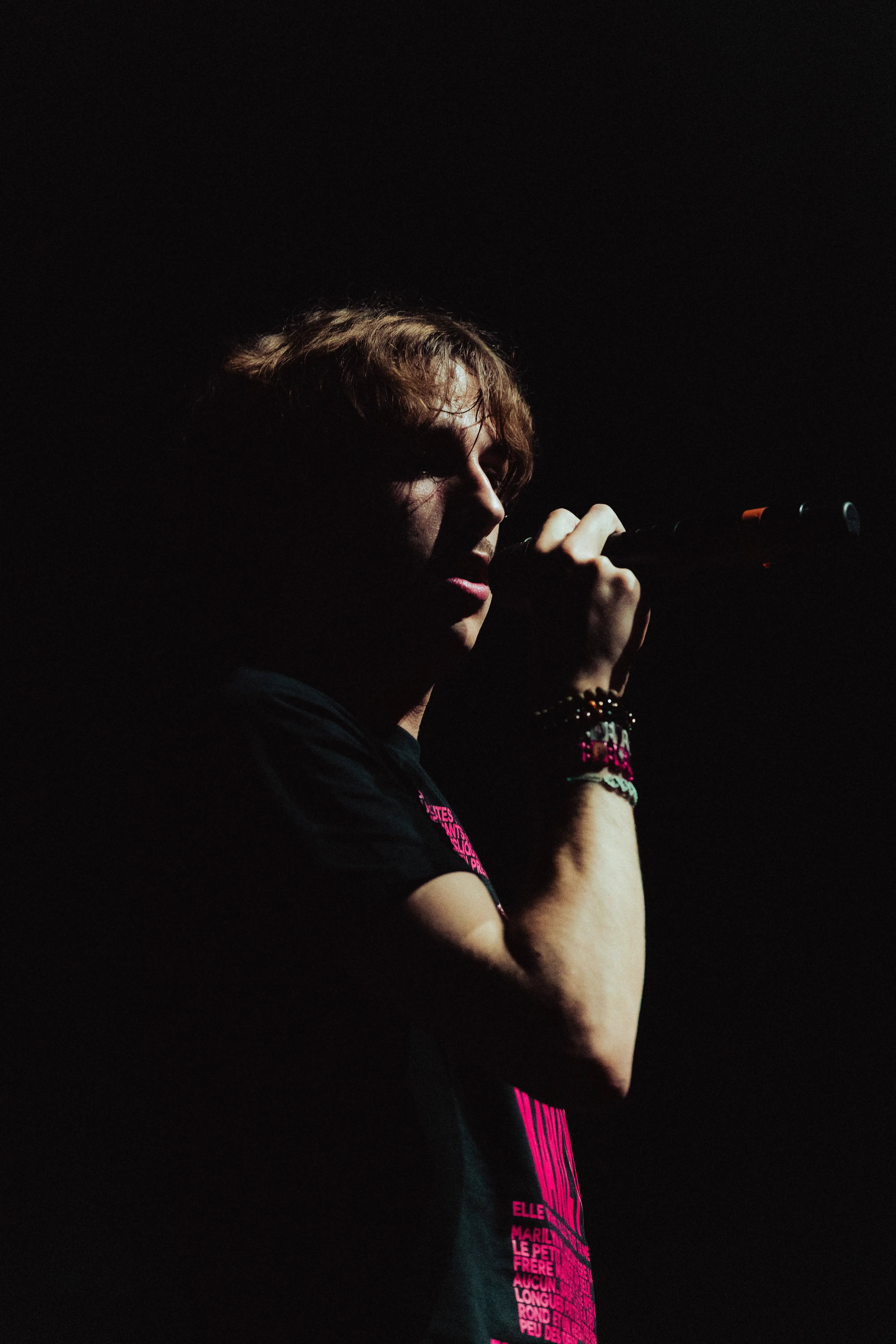 Un rappeur sur scène tenant un microphone, entouré d'un public levant des téléphones portables sous une lumière jaune intense.