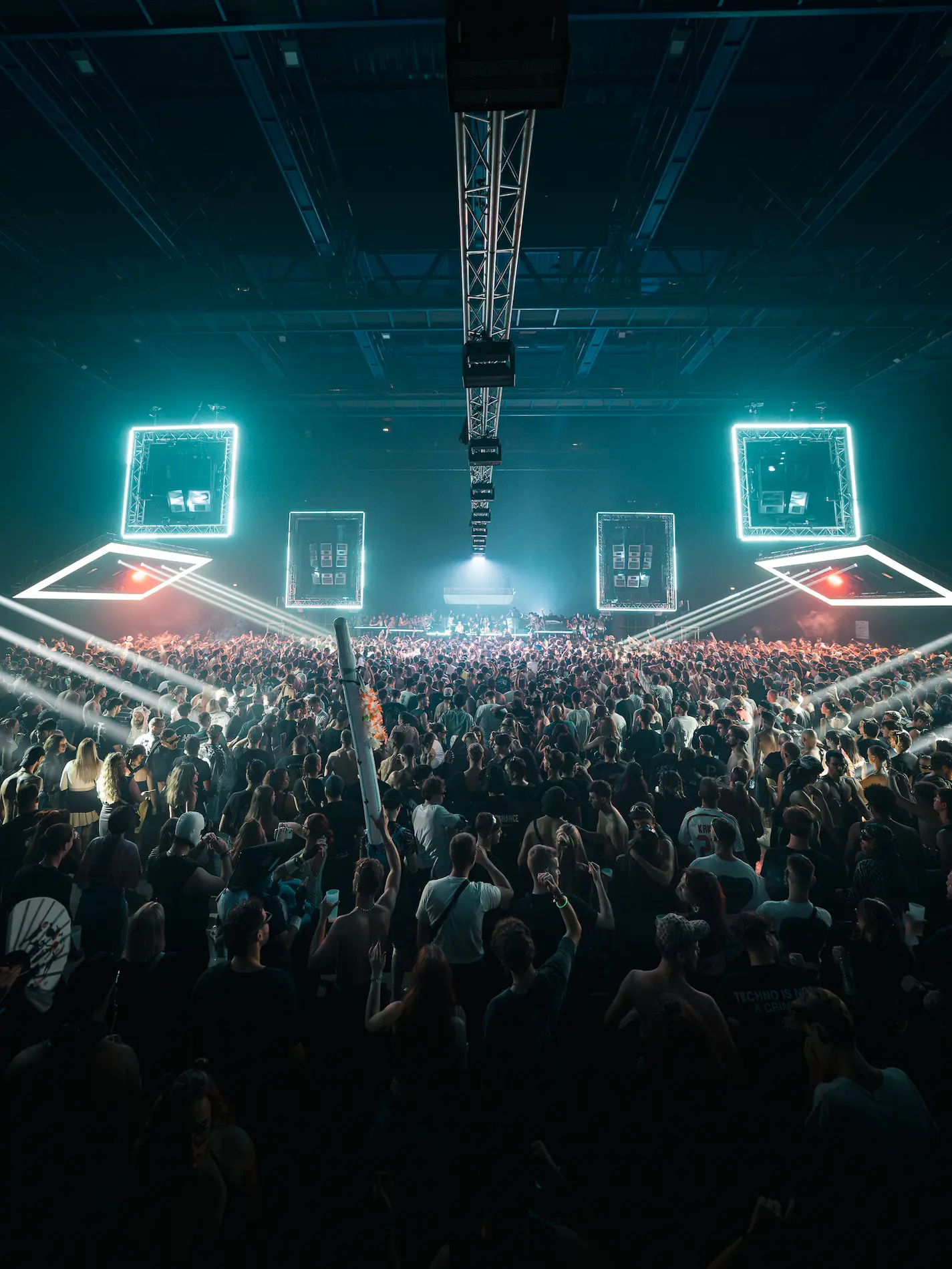 Un rappeur en sweat à capuche et bonnet debout au-dessus d'une foule avec des mains et des téléphones levés, fond jaune lumineux.