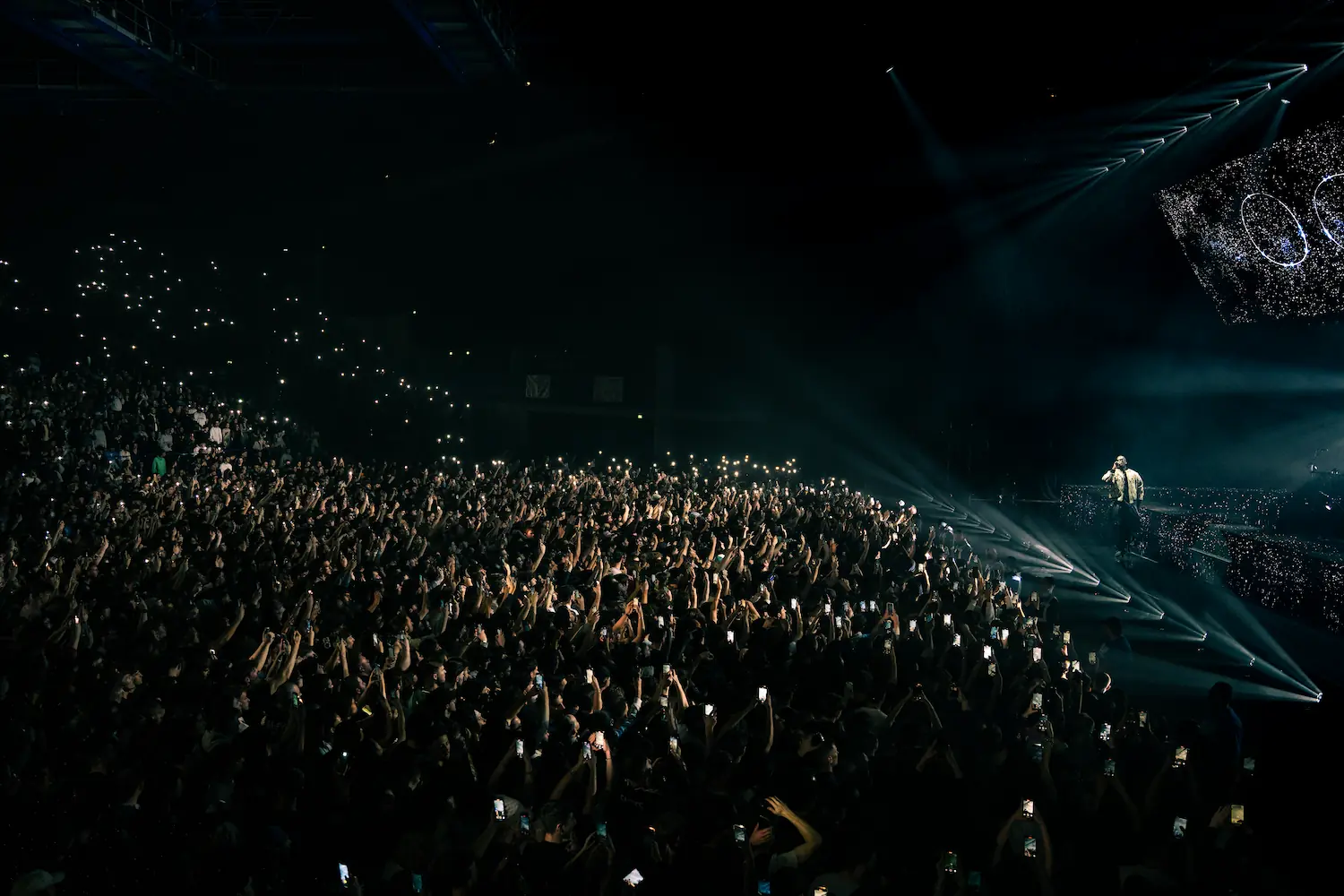Foule dense et enthousiaste lors d'un concert avec des gens tenant des téléphones portables levés.