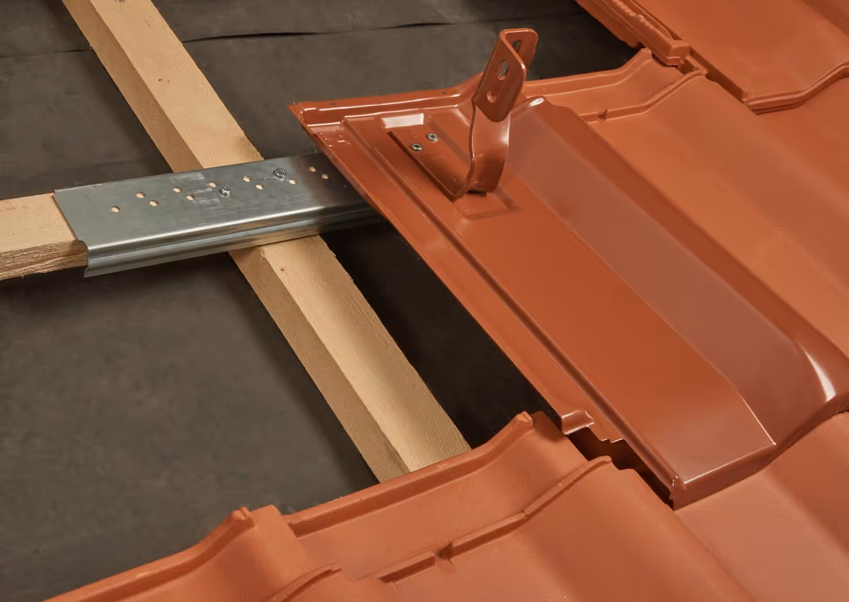 Nahaufnahme einer Terrakotta-Dachpfanne mit Befestigungshaken auf einer Holzlatte und Metallhalterung.