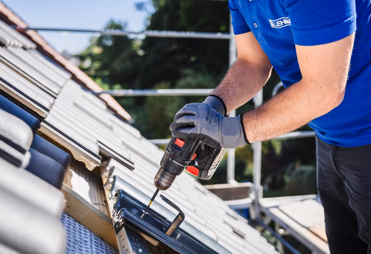 Handwerker verwendet Akkuschrauber zum Befestigen von Dachziegeln auf einem geneigten Dach.