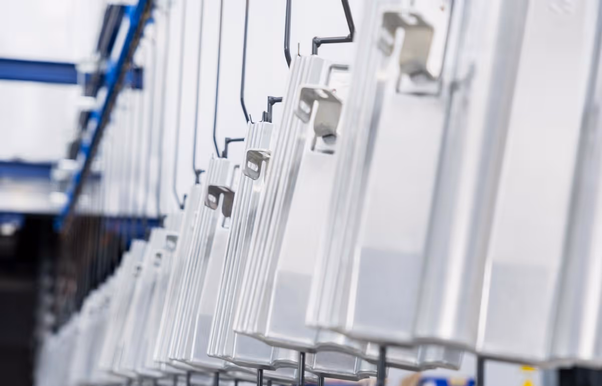 Reihe von feuerverzinkten Metallteilen, die an Haken in einer Produktionsstraße hängen.