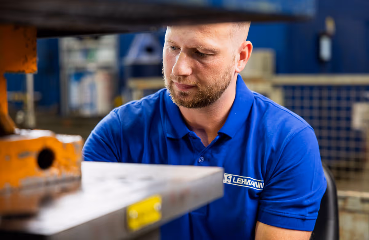 Mann in blauem Poloshirt mit Lehmann-Logo, der an einer Maschine in einer Werkstatt arbeitet.