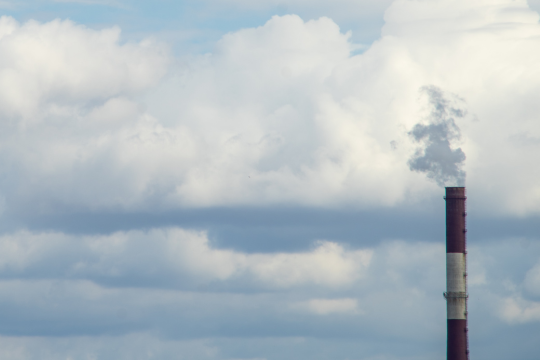 Das Bild zeigt einen Schornstein einer Fabrik, aus dem Rauch steigt