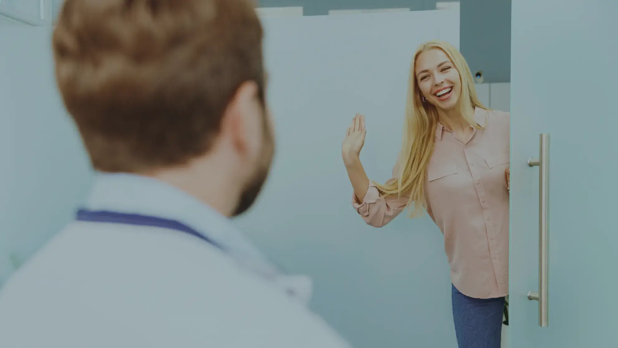 A woman opens a door and waves, smiling at a person in the foreground.