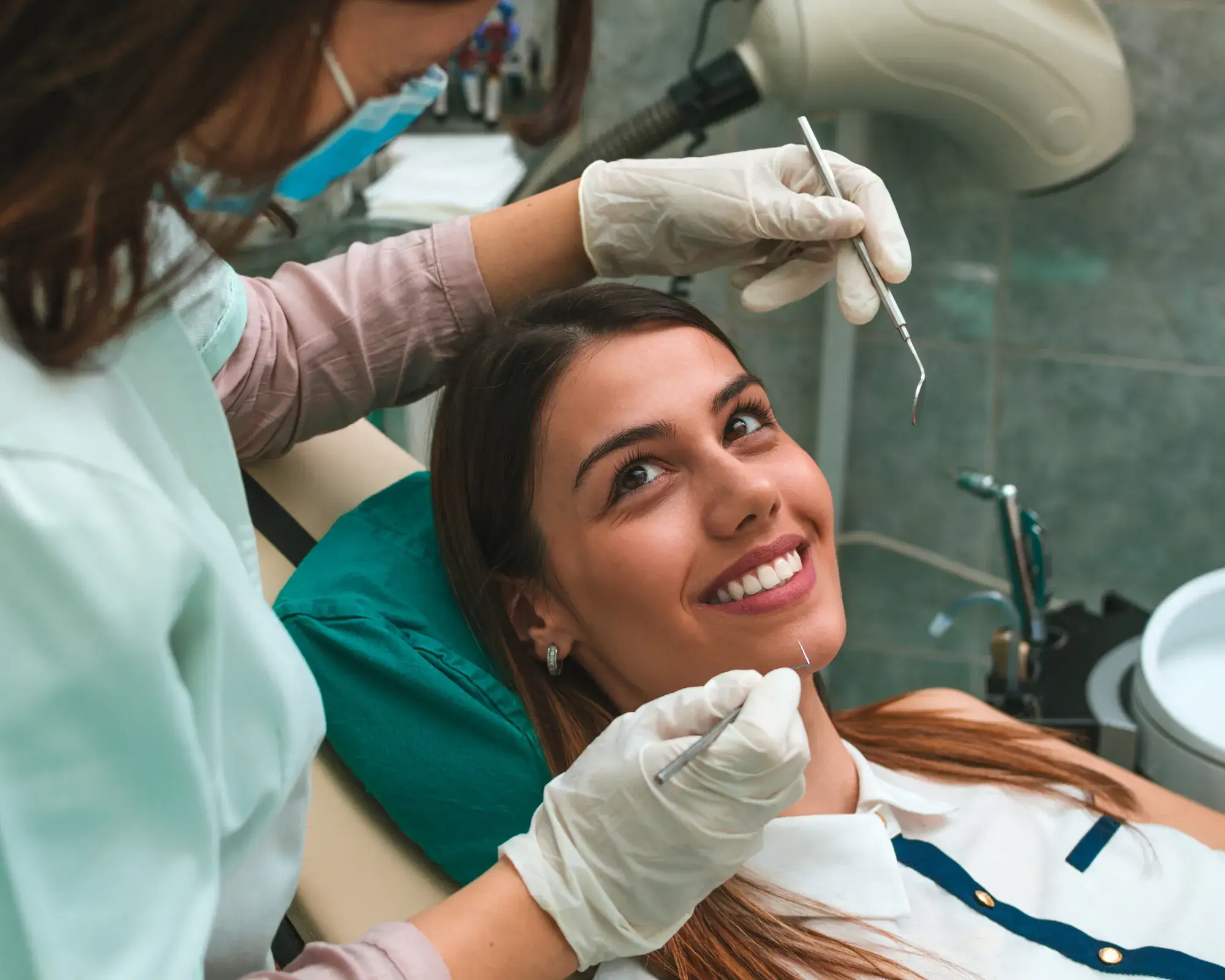 A dentist examines a smiling woman’s teeth in a dental office.