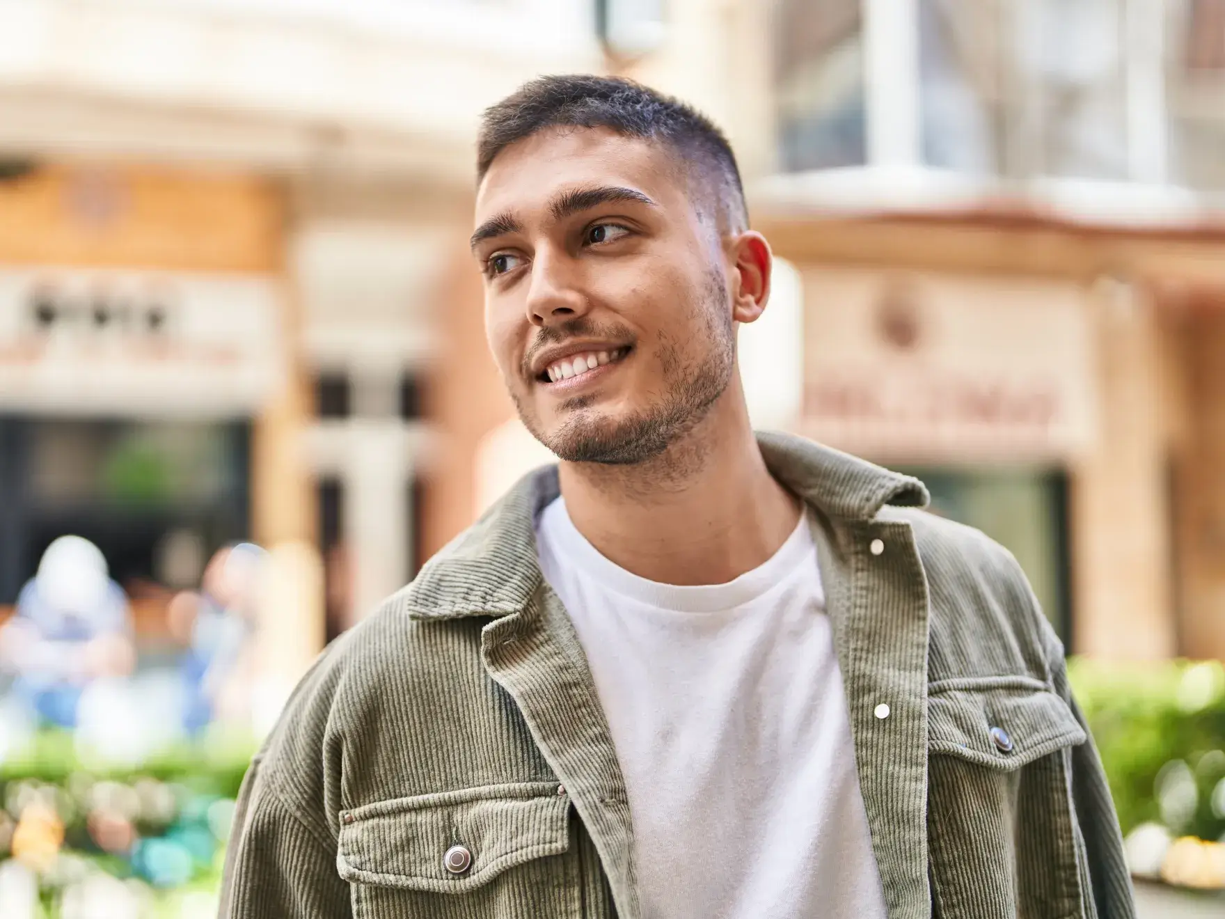 A man in a green jacket smiles while standing outside in a casual setting.