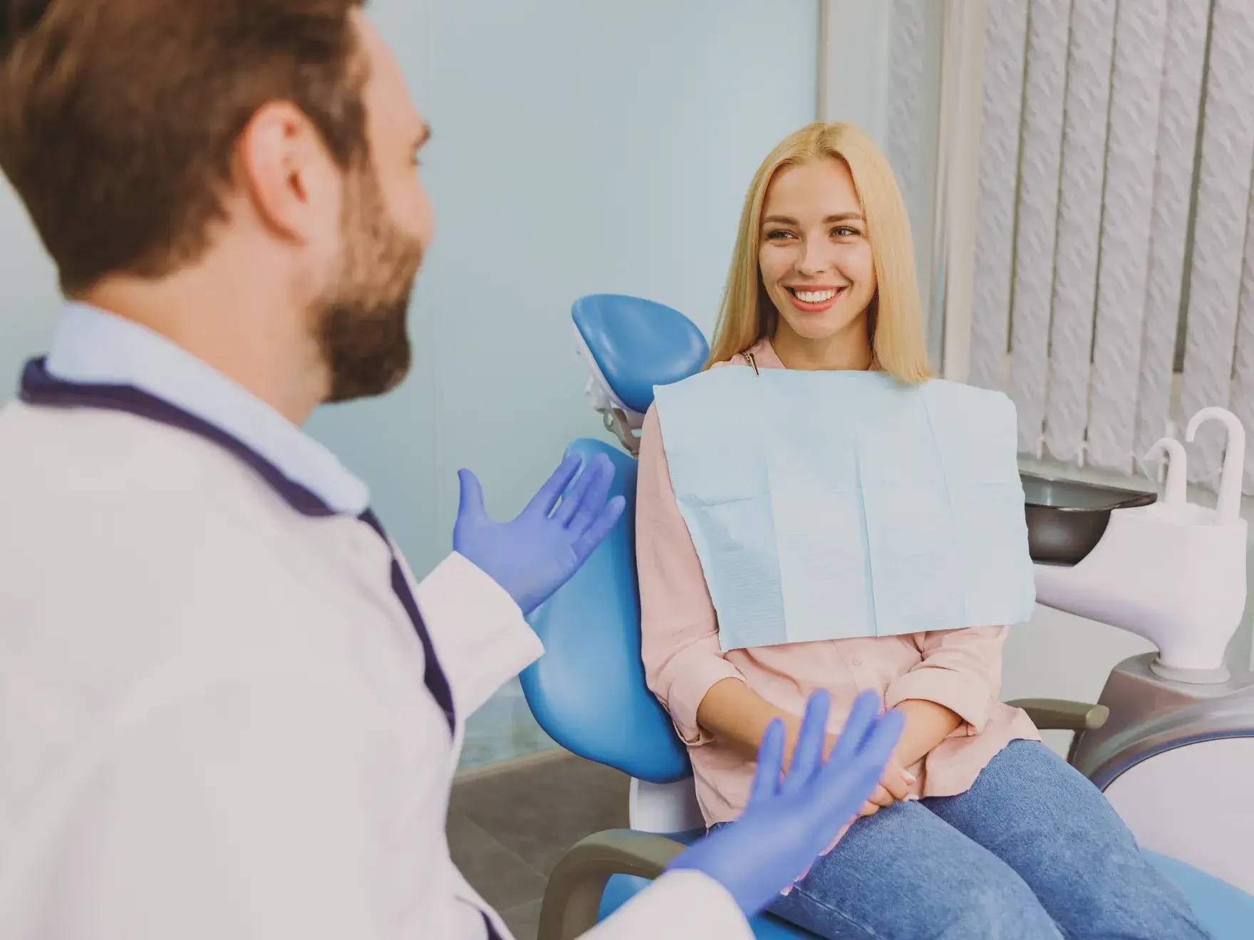Dentist talks to smiling woman sitting in a dental chair, both appear engaged and attentive.
