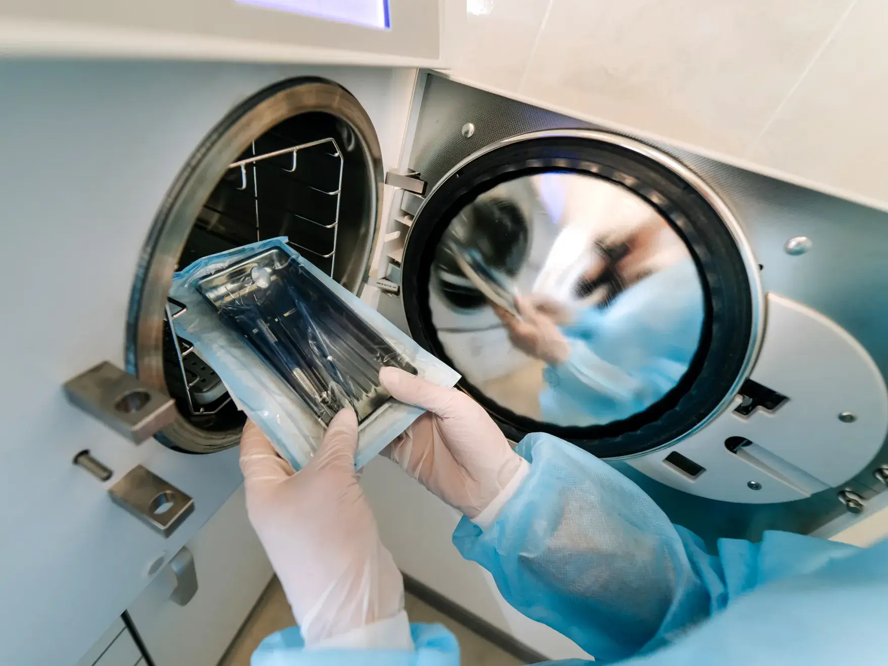 Person in gloves placing a bag of medical tools into a sterilization machine.