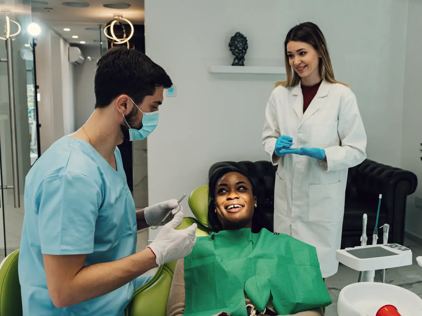 A dentist in scrubs and a dental assistant are preparing to treat a patient in a chair.