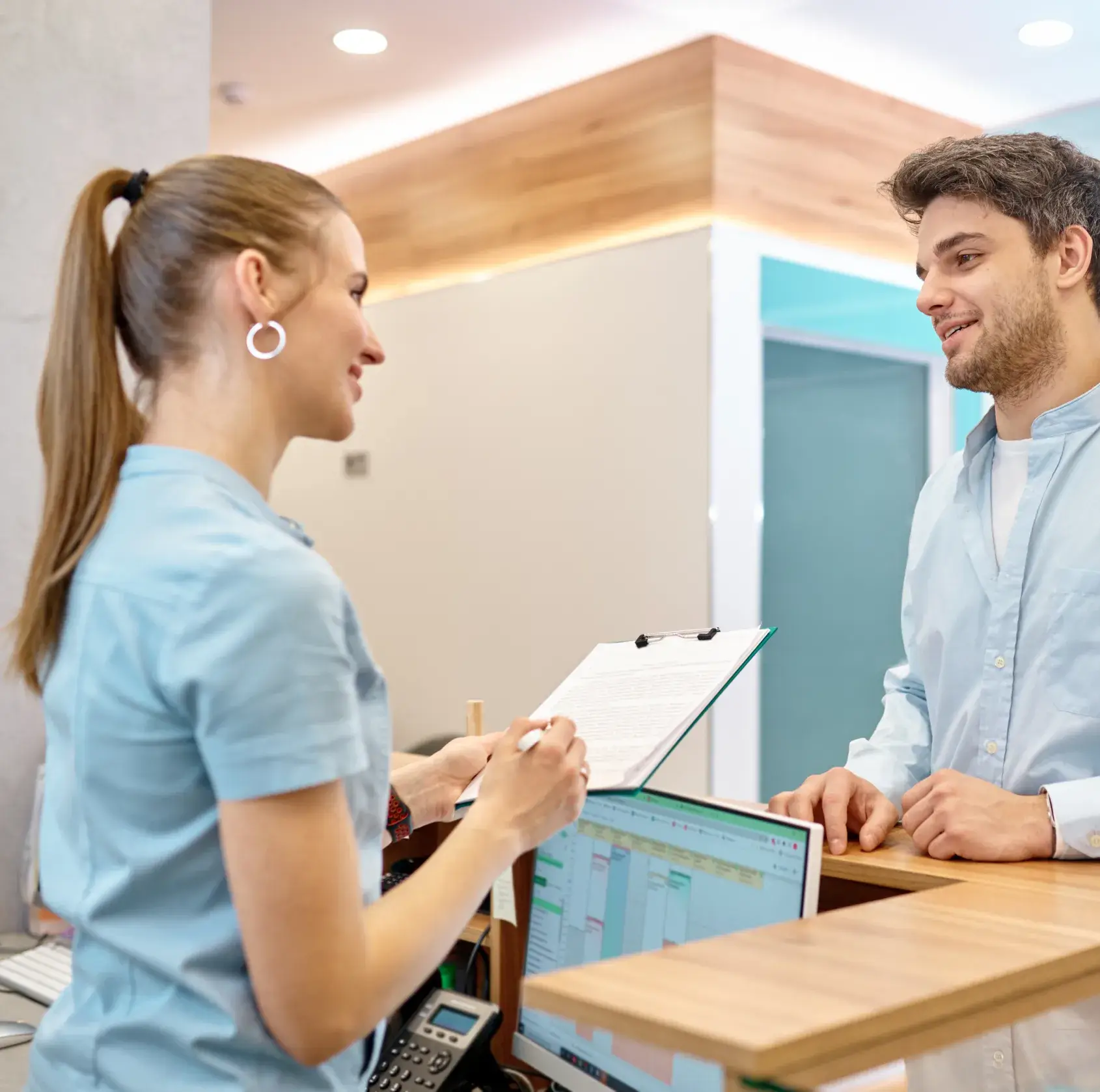 A receptionist hands a clipboard to a smiling man at a front desk.