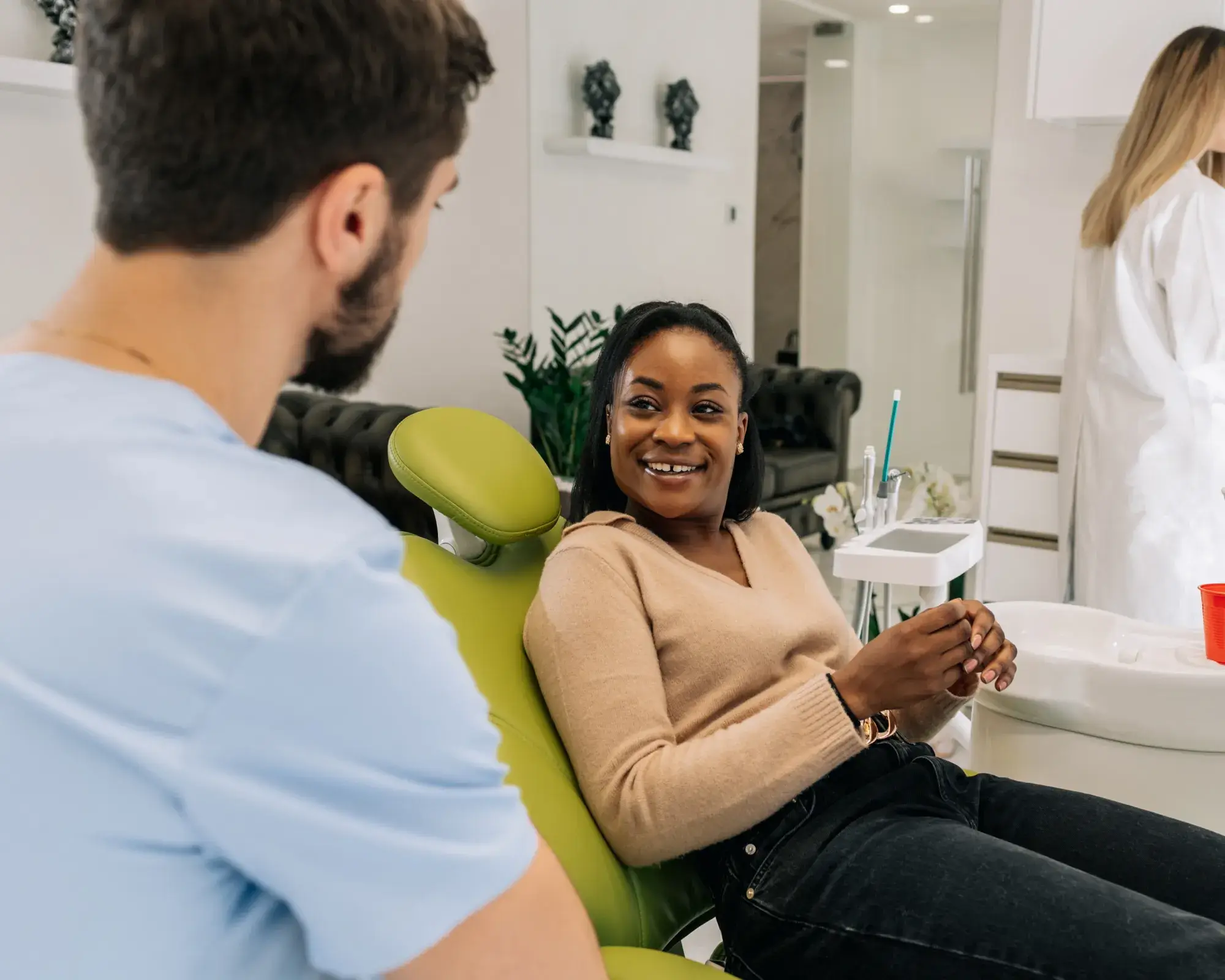 A woman sits in a dental chair, smiling at a dentist in a light blue shirt.