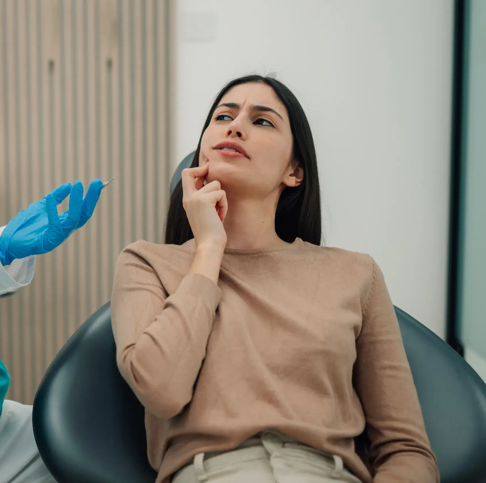 A woman sits in a dental chair, looking concerned, while a dentist holds a syringe.