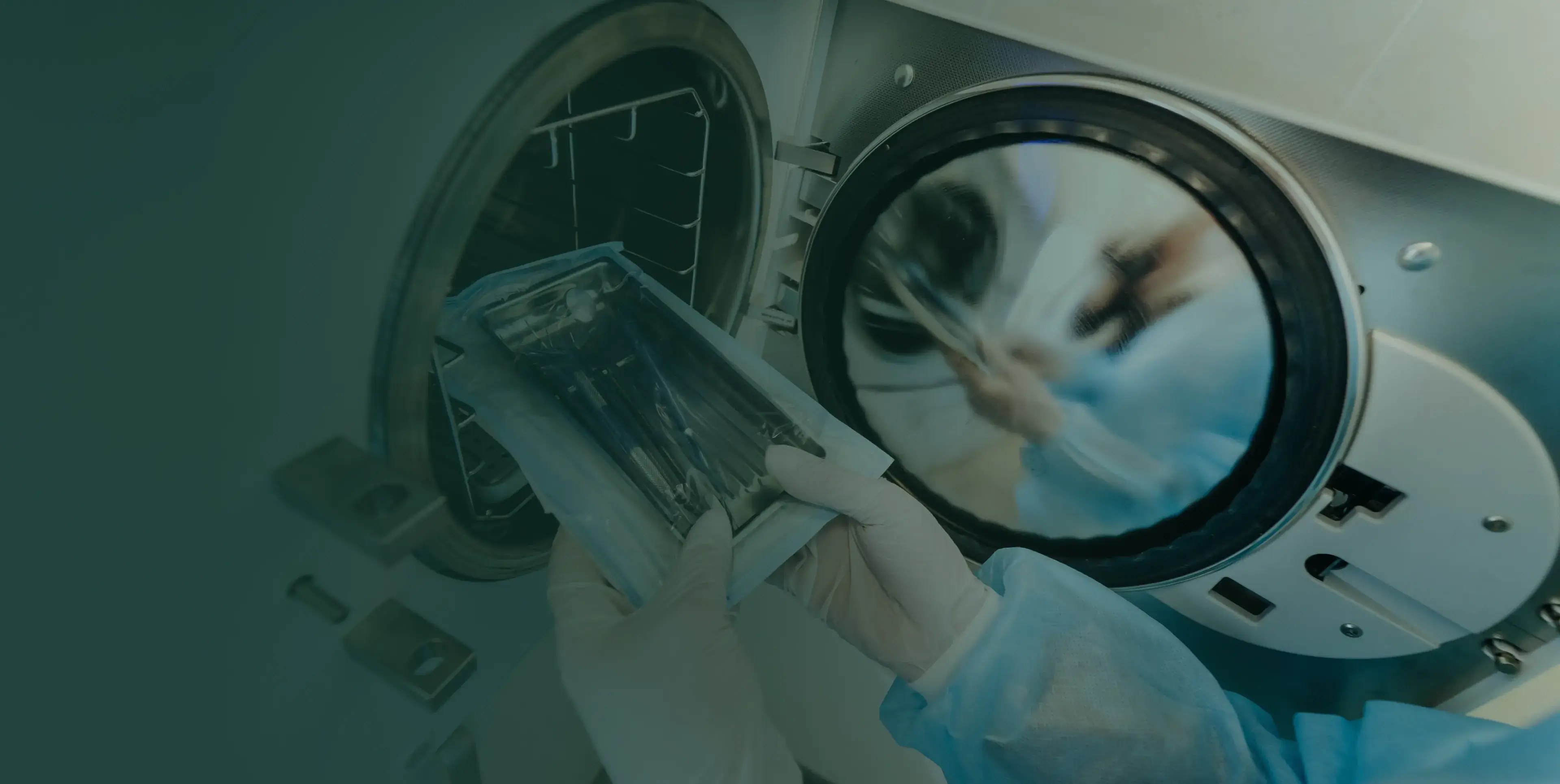 A person wearing gloves places medical instruments into a sterilization machine.