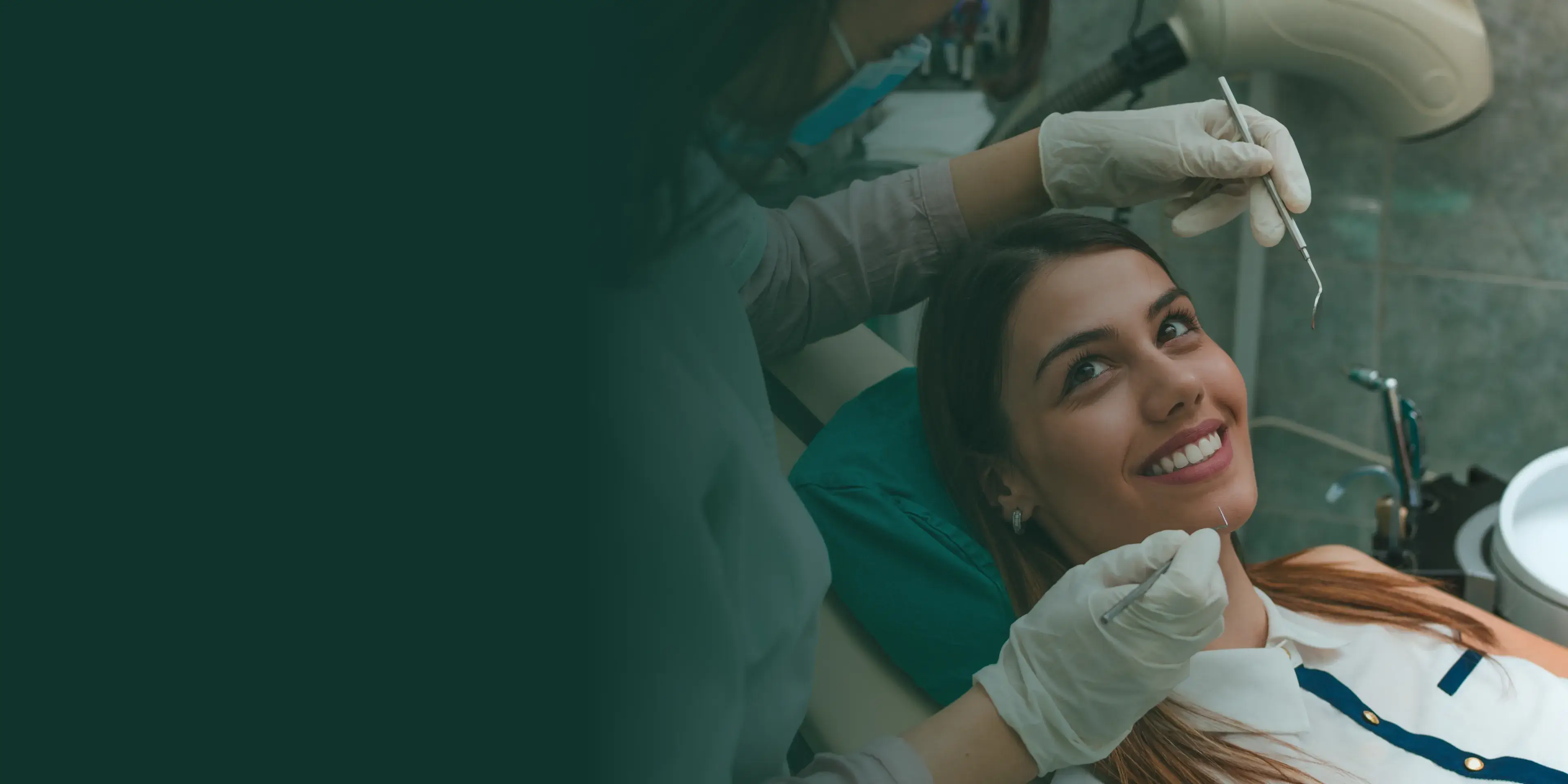 A dentist examines a smiling woman lying in a dental chair, using tools for an oral check-up.